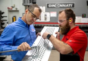 Ajax colleagues examining a fabricated tube sheet with extrusions using a micrometer.